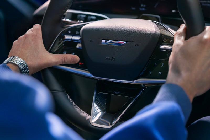 Close-up of a Man About to Press the V-Button on the 2026 OPTIQ-V Steering Wheel | Suttle Cadillac in NEWPORT NEWS VA